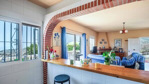 A kitchen with a wooden counter, two bar stools, a brick archway, and a dining area with a table and chairs. - Villa Los Peques (Torrox)