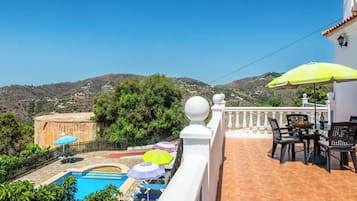 Zona de piscina con múltiples sombrillas, una mesa de comedor con sillas y vistas del paisaje circundante.