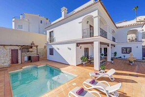Una casa de dos pisos con piscina, mobiliario exterior y un patio.