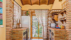 Une cuisine avec des murs en briques, un sol carrelé et une fenêtre ornée de rideaux à motifs floraux.