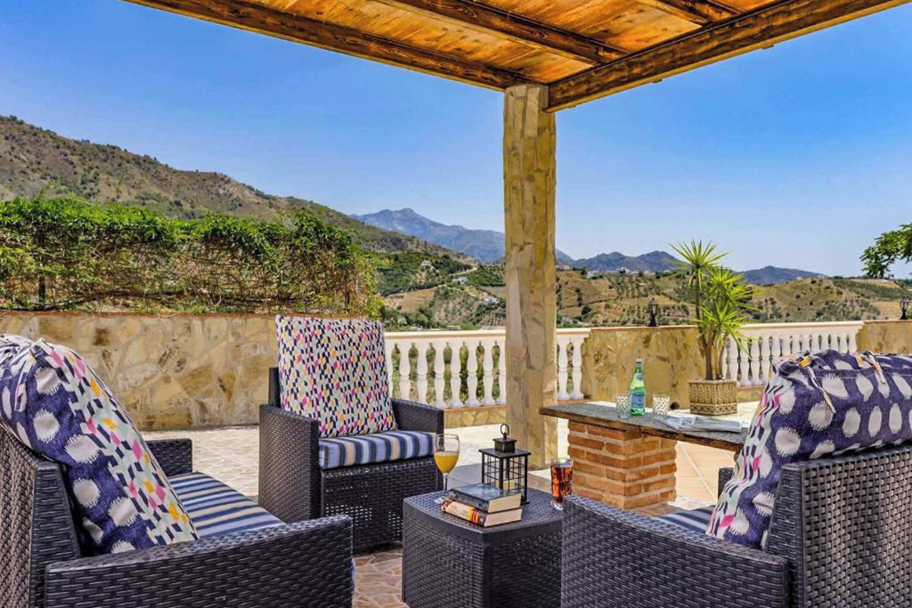Un espace extérieur aménagé avec des meubles en osier, une table avec des boissons, et une vue sur un paysage montagneux.