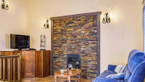 Un salon avec une cheminée en pierre, un canapé bleu, une table basse en bois avec des livres, un téléviseur et un meuble en bois.