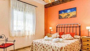 Une chambre à coucher avec un lit, une chaise, une table de chevet, une lampe et un tableau au mur.