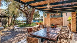 An outdoor patio with a wooden table and chairs, surrounded by stone walls and potted plants. - Villa Barbati Beachfront (Corfu)