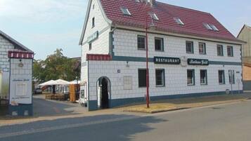 Een gebouw met twee verdiepingen, een betegelde gevel en een rood dak. Er hangt een bord dat aangeeft dat het een restaurant is, Balkan Grill.