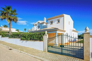 A white building with a tiled roof, a gated entrance, and a palm tree in the foreground. - Villa Beatrice (Albufeira)