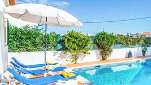 A poolside area with lounge chairs and umbrellas, surrounded by greenery and a clear blue sky. - Villa Julieta (Albufeira)