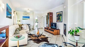 A modern living room with a sofa, coffee table, TV, and a glass table with a cowhide rug. - Villa Julieta (Albufeira)