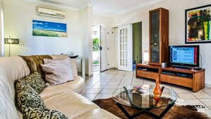 A living room with a sofa, a glass coffee table, a TV, and a painting on the wall. - Villa Julieta (Albufeira)