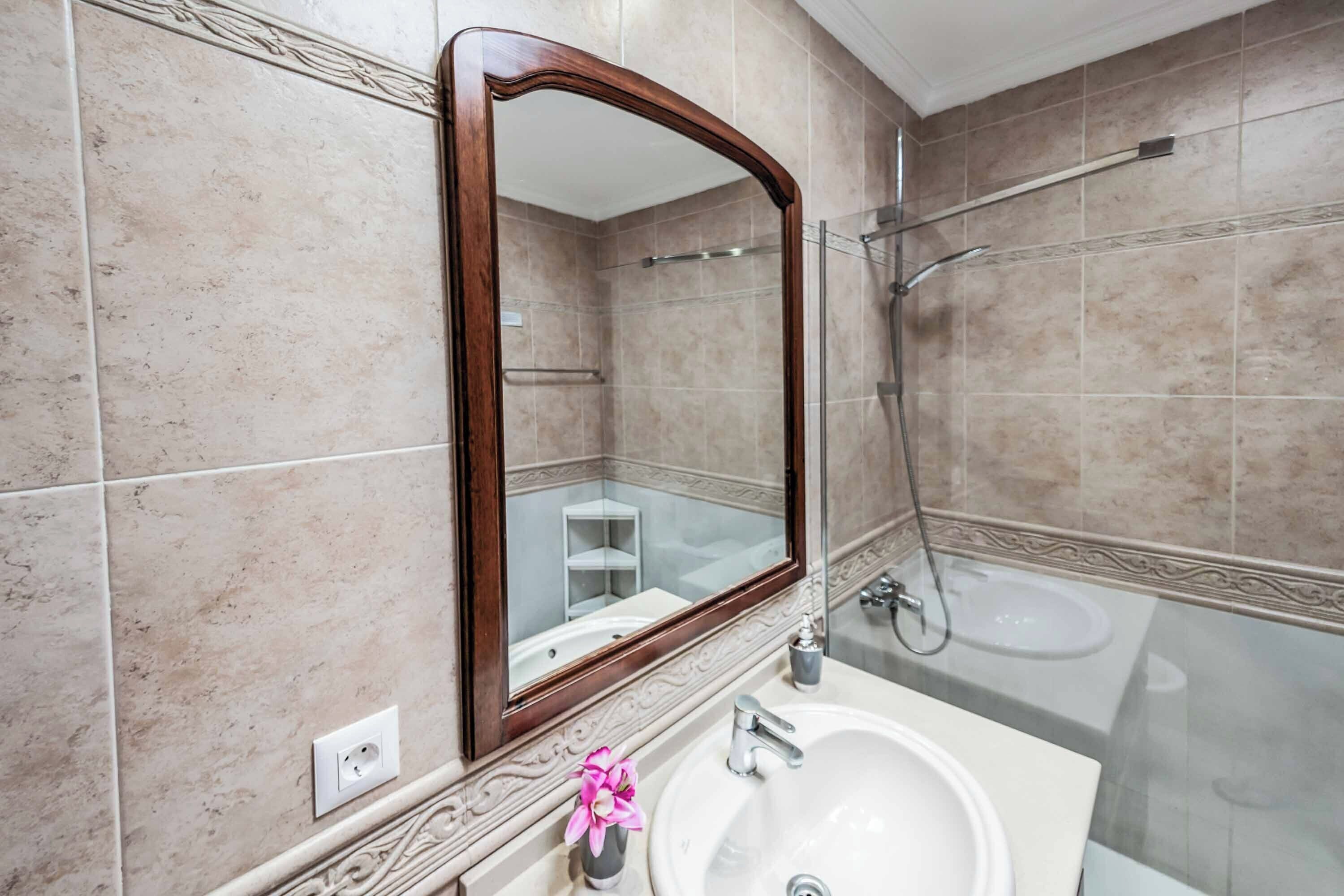 A bathroom with a large mirror, a sink, and a shower.