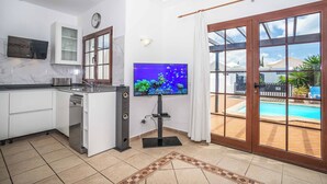 A modern kitchen with a built-in TV, a clock, and a view of a swimming pool. - Villa Emilia (Yaiza)