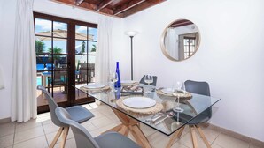 A dining area with a glass table, chairs, and a view of an outdoor pool. - Villa Emilia (Yaiza)