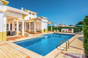 A swimming pool with a tiled deck, lounge chairs, and a covered seating area.