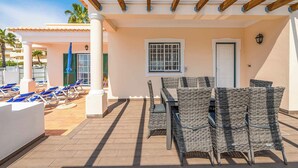 An outdoor patio area with wicker furniture, a pergola, and a poolside lounge with blue chairs. - Villa Minerva (Albufeira)