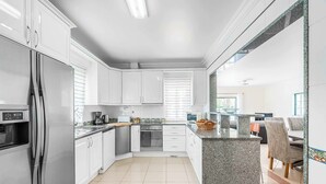 A modern kitchen with white cabinets, a stainless steel refrigerator, and a granite island. - Villa Minerva (Albufeira)