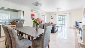 A modern kitchen with a dining area, a large window, and a flat-screen TV. - Villa Minerva (Albufeira)