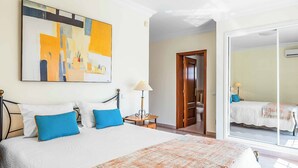 A hotel room with a large bed, a painting on the wall, a lamp, and a view through a glass door. - Villa Minerva (Albufeira)