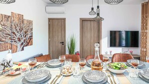 A dining room with a large table set for a meal, surrounded by chairs, and a television mounted on the wall. - Villa Eleonas (Rethymno)