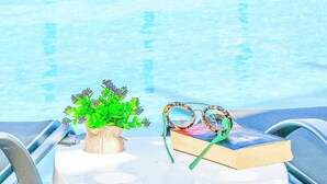 A poolside setting with a potted plant, a pair of sunglasses, and a book on a table. - Villa Eleonas (Rethymno)