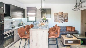 A modern kitchen with a central island, bar stools, a dining table set for four, and a living area with a sofa and coffee table. - Villa Eleonas (Rethymno)