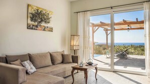 A living room with a beige sofa, a wooden coffee table, and a painting of a tree. - Villa Elaion (Kefalonia)