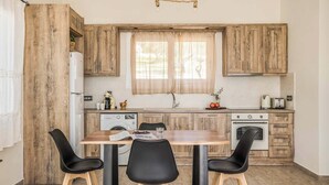 A kitchen with wooden cabinets, a dining table with chairs, a washing machine, and a window with curtains. - Villa Elaion (Kefalonia)