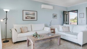 Una sala de estar con dos sofás blancos, una mesa de centro de madera, una lámpara de pie y cuadros enmarcados en la pared.