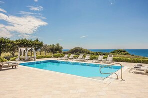 A rectangular swimming pool with a clear blue water, surrounded by lounge chairs and a pergola. - Villa Alba Minies (Kefalonia)