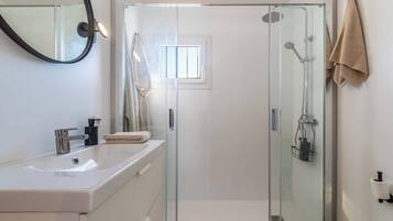 Un baño moderno con cabina de ducha de vidrio, un lavamanos blanco y un perchero para toallas.