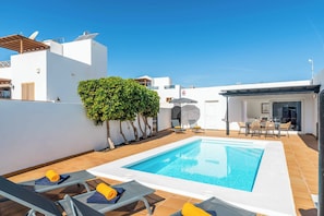 A rooftop pool area with lounge chairs, a small table, and a covered seating area.