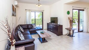 A modern living room with a sectional sofa, a wooden coffee table, a TV, and a dining area with a small table and chairs. - Villa Lara Latchi (Polis)