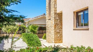 A modern building with a stone facade, a window, and a well-maintained garden with various plants and a gravel path. - Villa Lara Latchi (Polis)