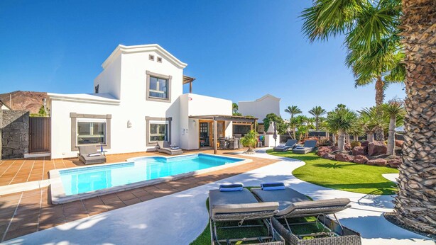 A modern house with a swimming pool, outdoor seating, and palm trees. - Villa Lucero (Yaiza)