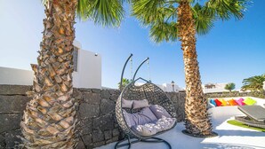 A hanging chair in a sunny outdoor area with palm trees and a stone wall. - Villa Lucero (Yaiza)