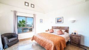 A bedroom with a bed, a nightstand, a lamp, a sofa, and a window with a view. - Villa Lucero (Yaiza)