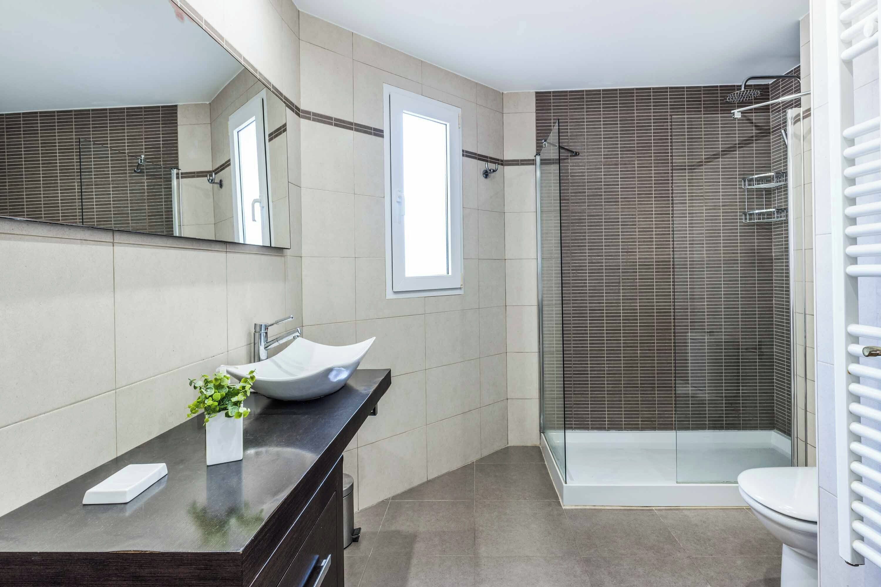 A modern bathroom with a large mirror, a vessel sink, a glass shower enclosure, and a toilet.