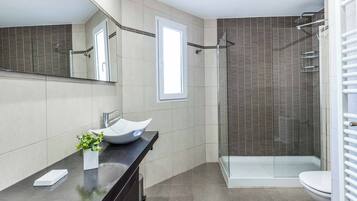 A modern bathroom with a large mirror, a vessel sink, a glass shower enclosure, and a toilet.