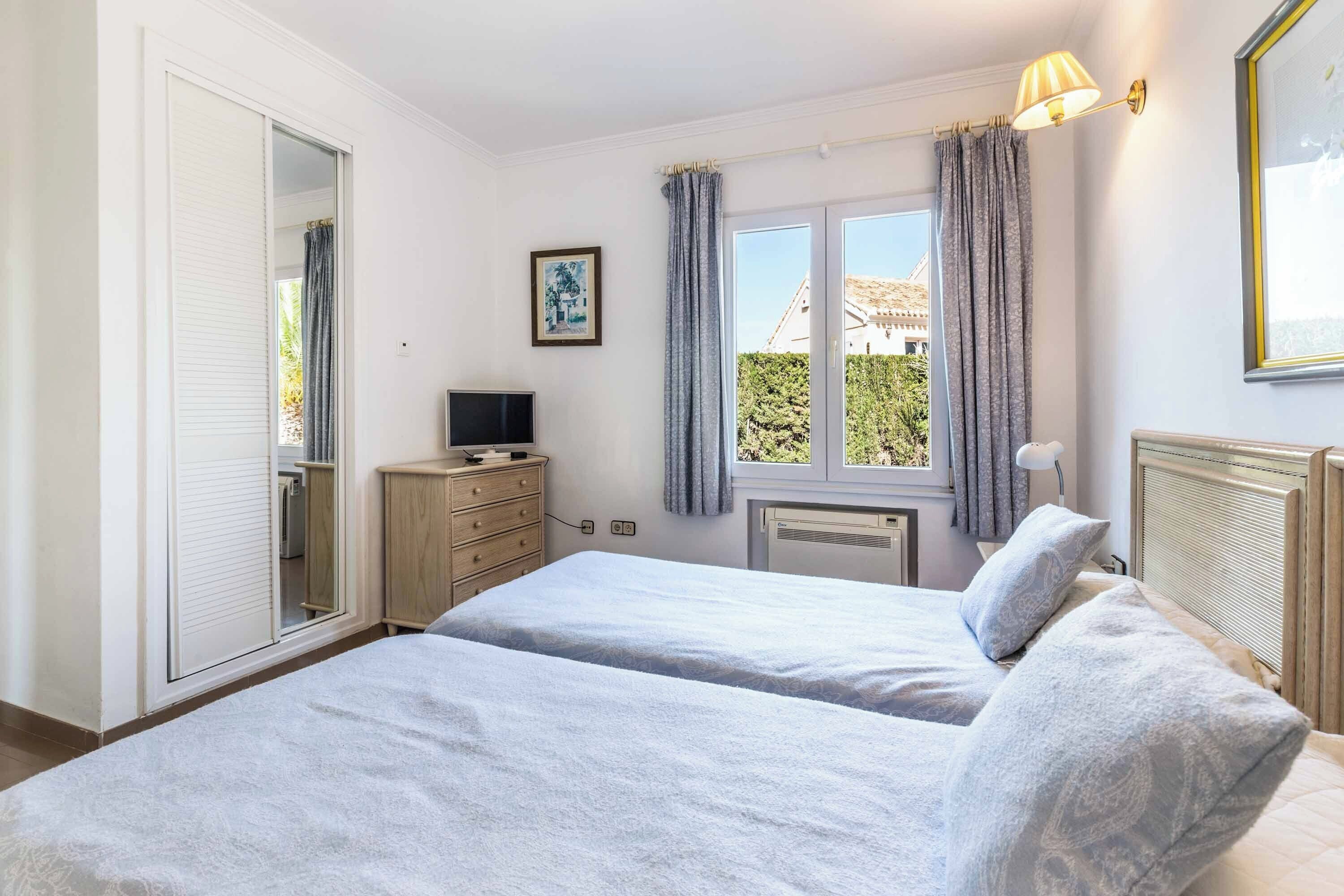 A bedroom with two beds, a TV, a dresser, and a window with curtains.