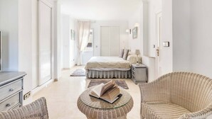A bedroom with a bed, a bedside table, a lamp, a wicker chair, a glass table with a book, and a wardrobe. - Villa Las Brisas 87 (Cartagena)
