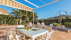 An outdoor patio with a glass table and chairs, surrounded by potted plants and a view of a mountain. - Villa Las Brisas 87 (Cartagena)