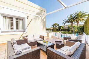 An outdoor patio with wicker furniture, a glass table, and a view of a swimming pool and palm trees. - Villa Las Brisas 87 (Cartagena)