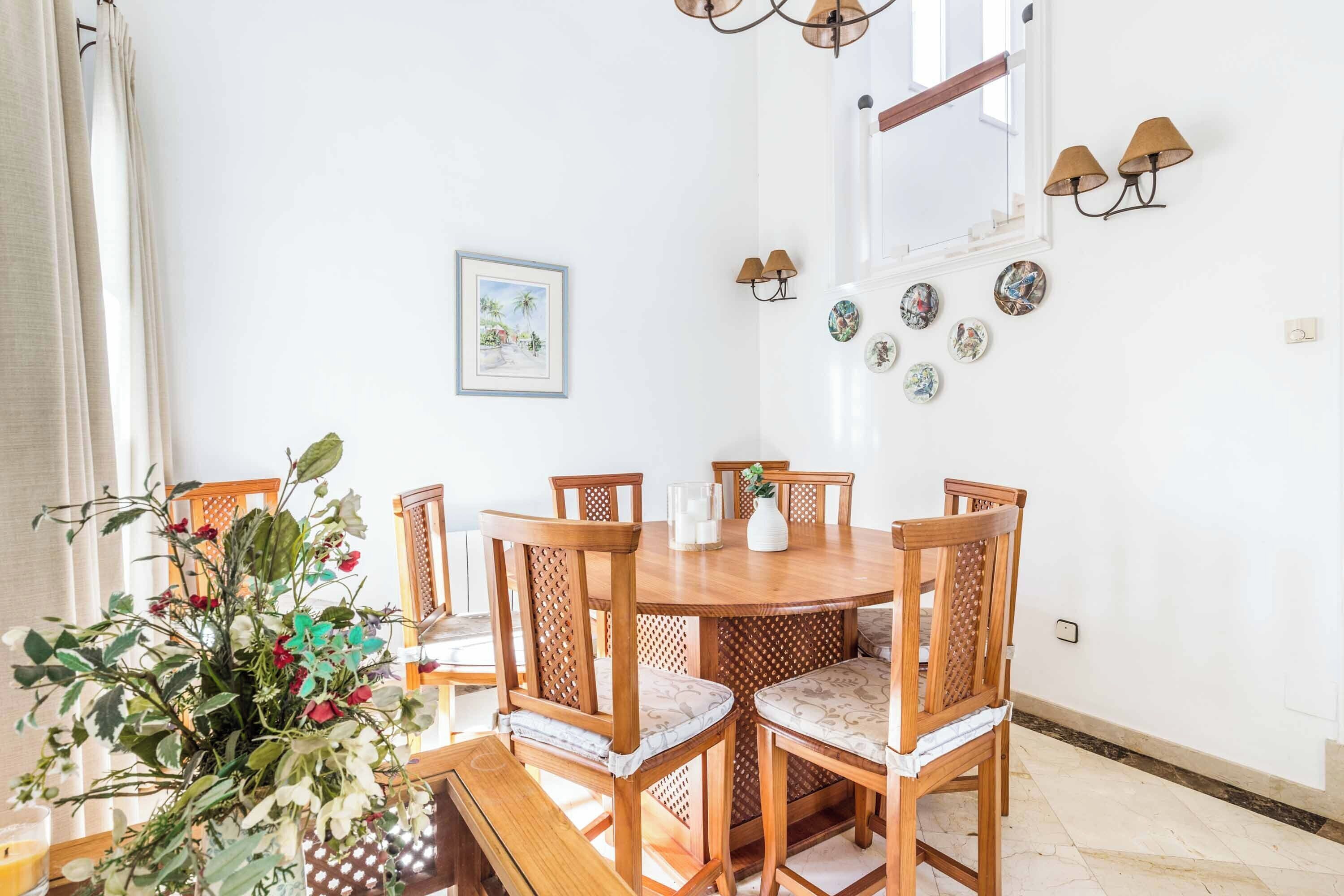 Un comedor con una mesa y sillas de madera, un jarrón de flores y platos decorativos colgados en la pared.