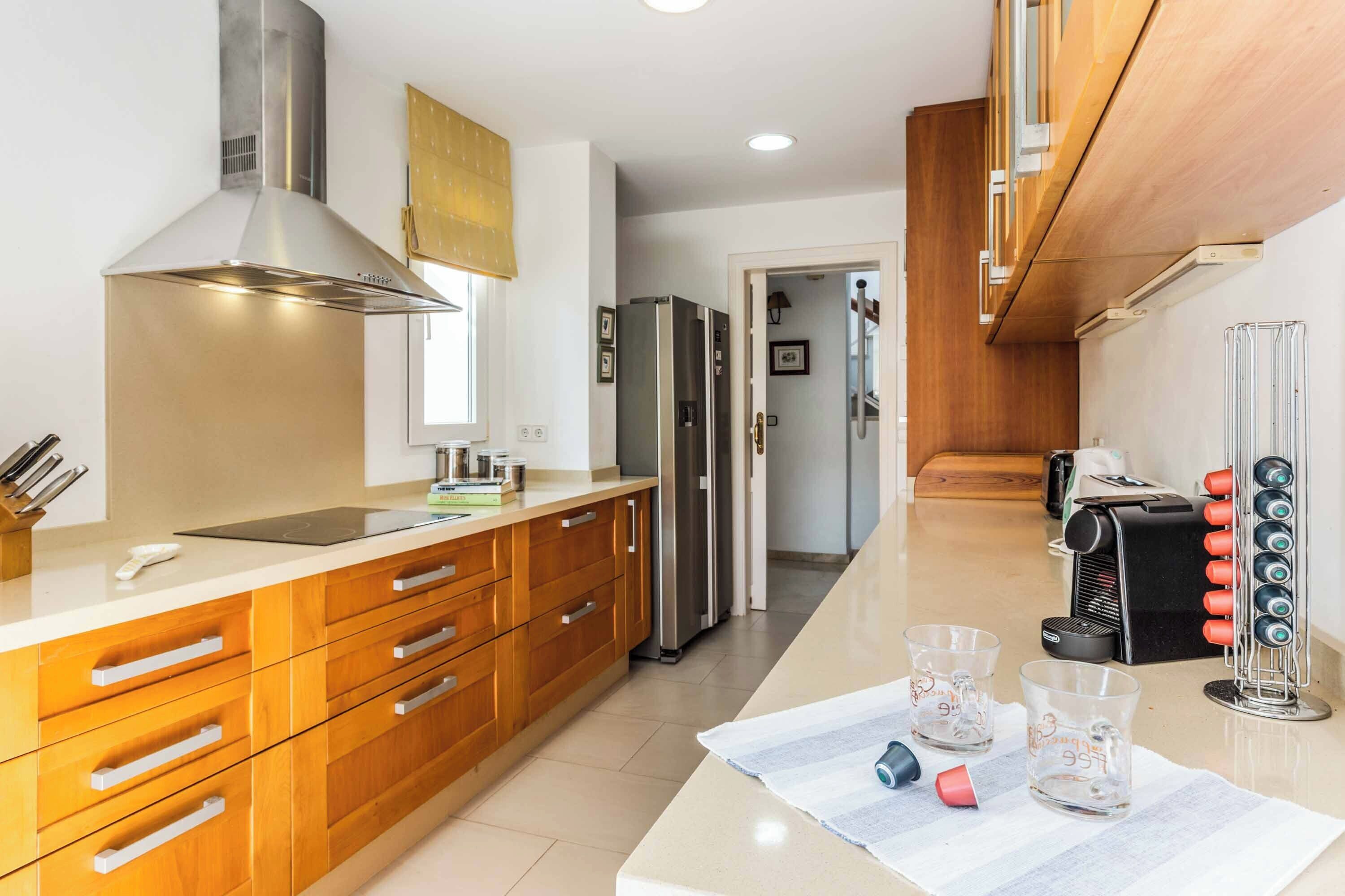 A modern kitchen with wooden cabinets, a stainless steel range hood, a refrigerator, and a coffee machine.