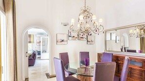 Un coin repas avec une table en verre, des chaises violettes, un buffet en bois et un lustre.