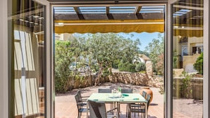 Une terrasse extérieure avec une table et des chaises, entourée d’un mur de pierre et de verdure.