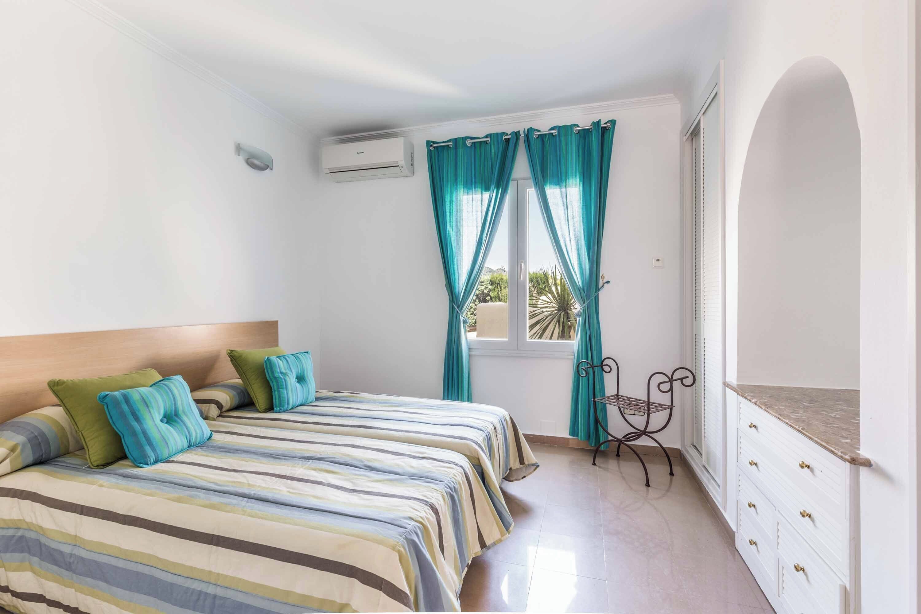 Un dormitorio con dos camas, una ventana con cortinas, una mesita y un armario.