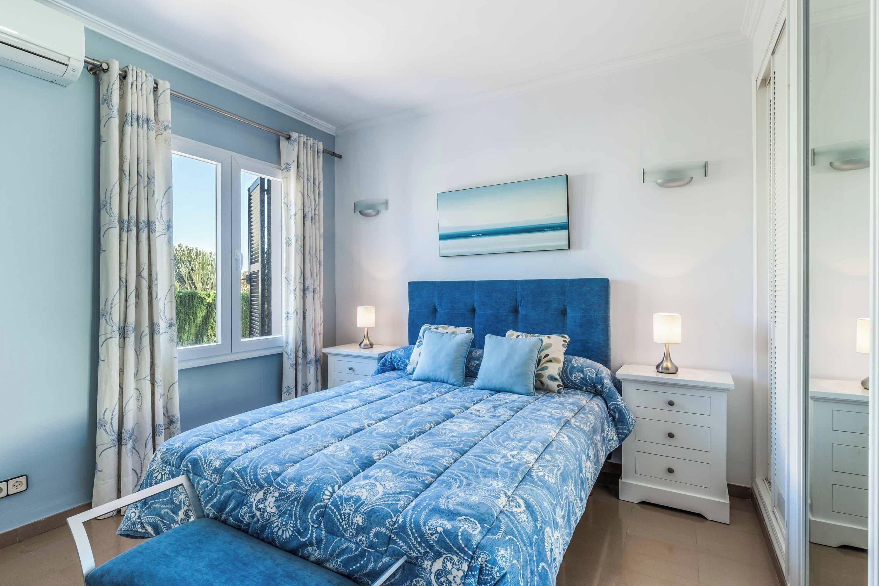 A bedroom with a large bed, two bedside tables, a window with curtains, and a painting on the wall.