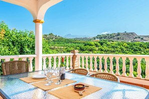 A table set with wine glasses and a bowl of olives on a balcony with a white railing and a view of a lush landscape. - Villa Carmela Nerja (Nerja)