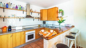 A kitchen with wooden cabinets, a marble countertop, a built-in oven, a microwave, and a coffee machine. - Villa Carmela Nerja (Nerja)