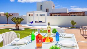 Mesa de jantar posta ao ar livre, com vista para um edifício moderno, uma palmeira e céu claro.